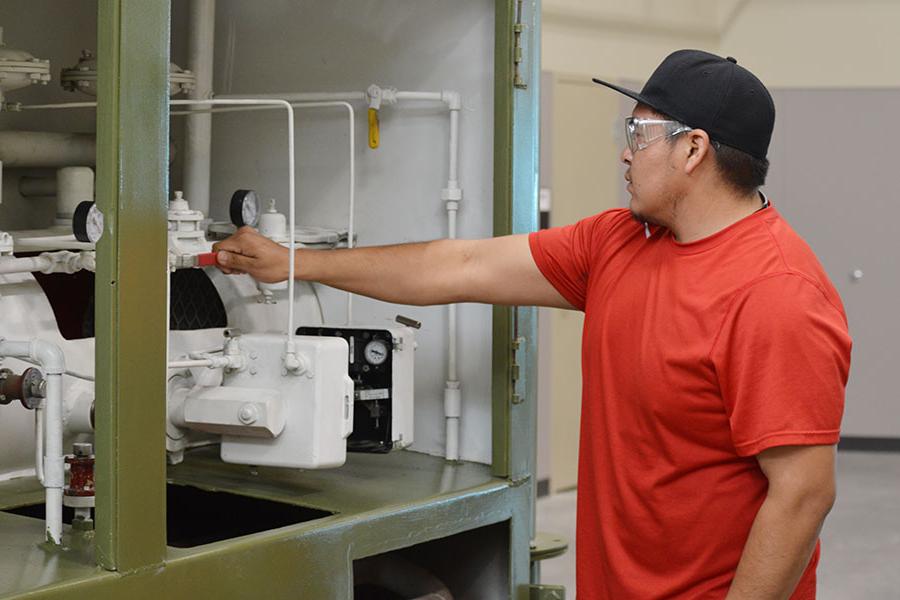 An individual wearing a hat and safety goggles turns the valve on production machinery